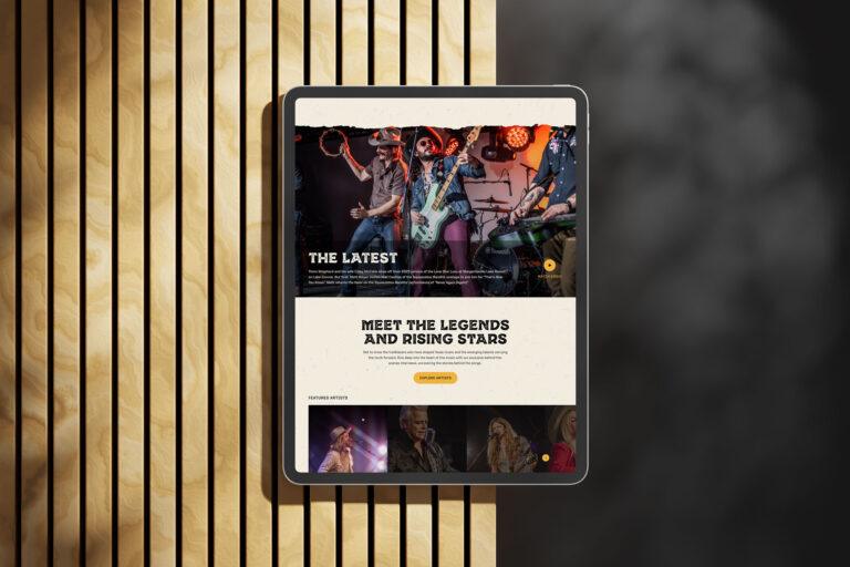 A tablet displaying a music-themed website featuring the Texas Music Scene, with images of performers on stage, headlines reading “The Latest” and “Meet the Legends and Rising Stars,” placed on a light wooden surface with vertical slats.