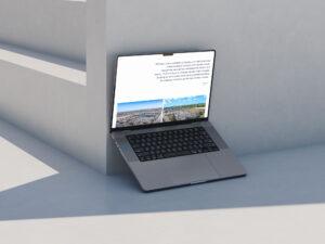 A laptop with a black keyboard is propped open against a white concrete wall in bright sunlight. The screen displays text and photos of an urban landscape. Shadows and clean lines create a minimalist, modern scene.