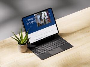 A tablet with a keyboard on a wooden desk displays a website with the text “Looking for an Expert?” next to a small potted succulent, seamlessly blending digital work and Stream Reality.