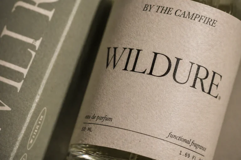 A close-up of a perfume bottle labeled WILDURE with the phrase BY THE CAMPFIRE printed above. The minimalist label also reads eau de parfum and functional fragrance. | Terrain