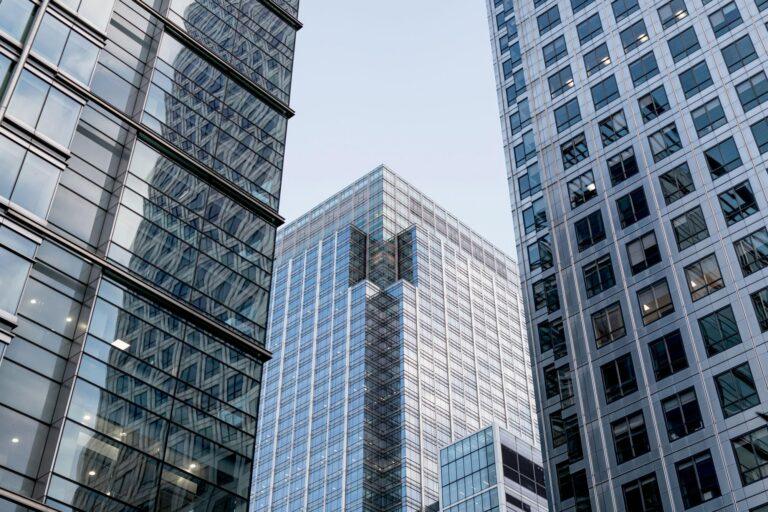 Tall modern office buildings with glass and steel exteriors rise against a clear sky, reflecting each other in their windows. The symmetrical architecture creates a geometric urban scene ideal for a commercial real estate website. | Terrain
