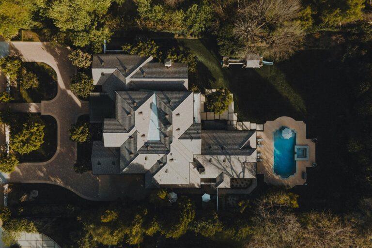 Aerial view of a large house with a gray roof, surrounded by trees and greenery, featuring a driveway, pathways, and a backyard swimming pool—much like deciding how to choose a web design agency for your perfect online presence. | Terrain