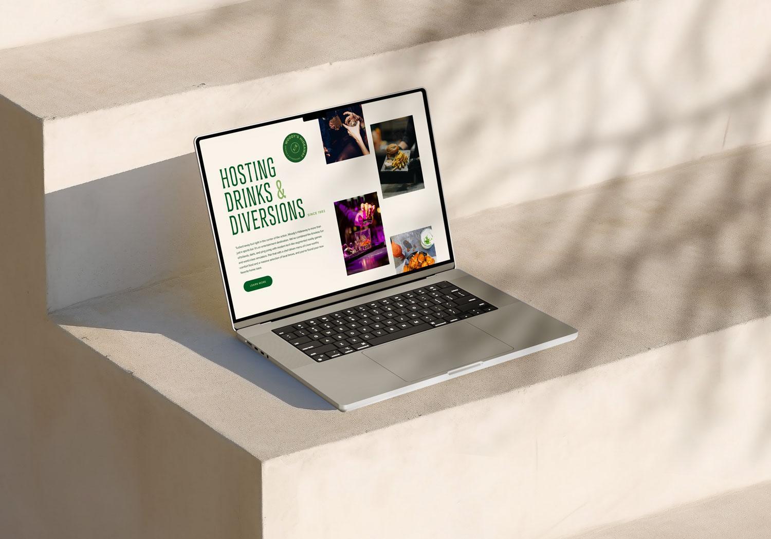 A laptop on sunlit stone steps displays a website with the heading Hosting Drinks & Diversions, featuring photos of drinks, food, and people socializing at Woody's Hideaway. Shadows from branches are cast across the steps. | Terrain